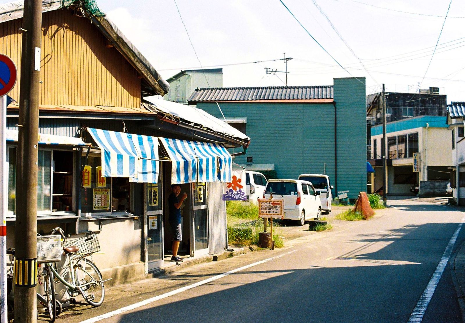 青白のしましまの日よけと氷ののぼりがある店先
